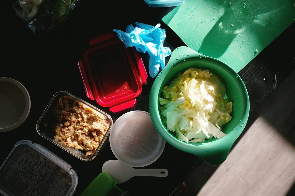 Colorful gut healthy meal prep containers with kimchi, cooled quinoa, steamed kale, and olive oil drizzle
